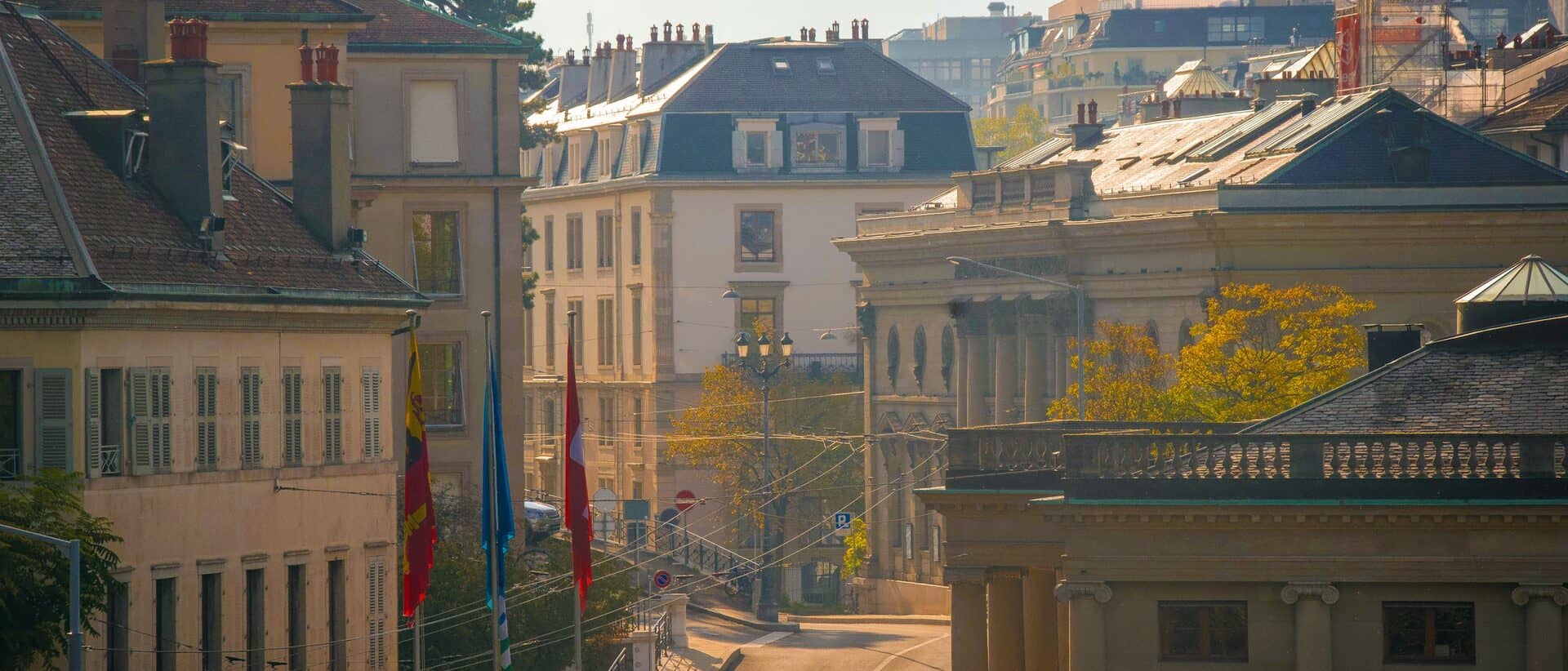 Architecture civile de la vieille ville de Genève en lumière dorée, drapeaux genevois et suisse.